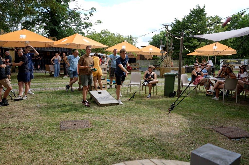 Buurtbewoners spelen cornhole en zitten samen aan de zomerbar onder parasols
